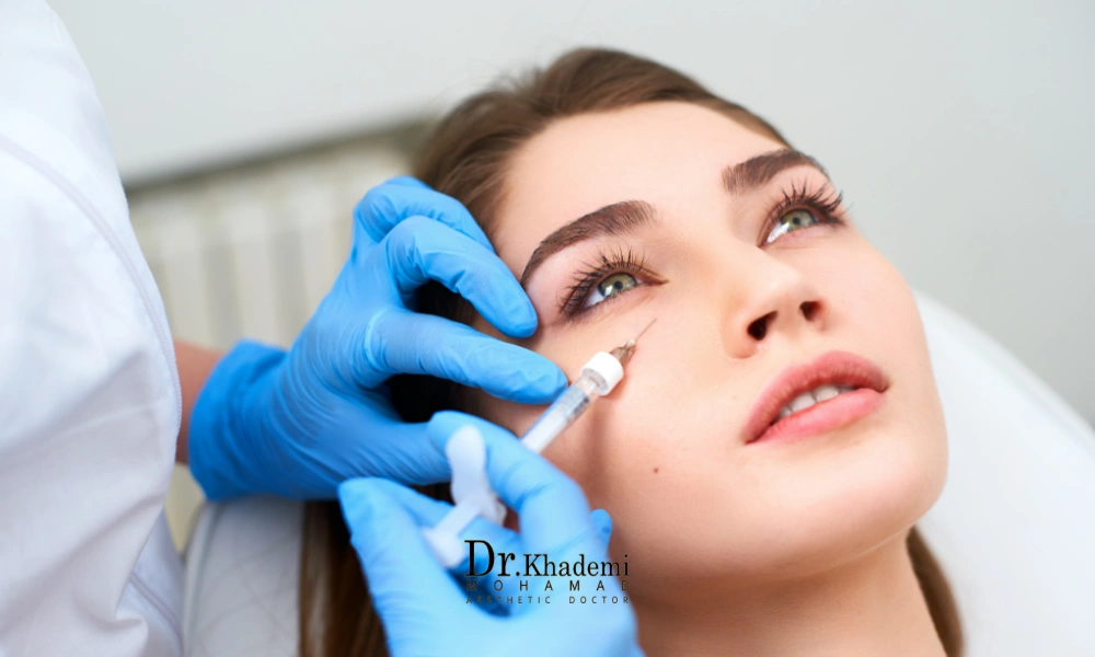 پزشک با دستکش های آبی در حال تزریق فیلر زیر چشم | کوچک شدن چشم با فیلر